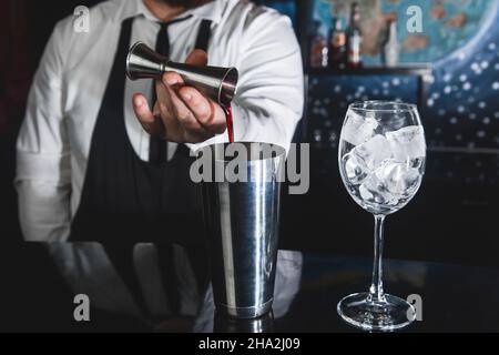 Les mains d'un barman professionnel versent le sirop dans un verre mesureur de jigger dans un outil métallique pour préparer et mélanger des cocktails alcoolisés de SH Banque D'Images