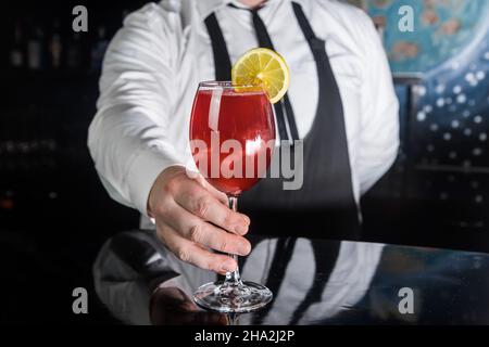 Le bar-salon professionnel sert des boissons alcoolisées rouges dans un cocktail en verre décoré d'une tranche de citron sur le comptoir du bar. Banque D'Images