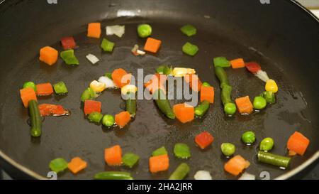 Remuez les légumes frits dans la casserole et les ingrédients en gros plan, la nourriture végétarienne.Poivron rouge en tranches, haricots verts, pois, maïs, oignons,carottes frites Banque D'Images