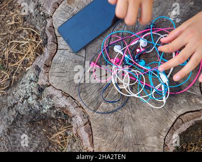 Un téléphone et une main tenant un nœud de quatre paires d'écouteurs intra-auriculaires filaires roses, bleus, blancs et noirs se sont emmêlés dans un problème désordonné. Banque D'Images