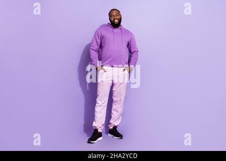 Vue sur toute la longueur du corps d'un joli gars plein de confiance et gai tenant les mains dans des poches isolées sur fond violet violet Banque D'Images