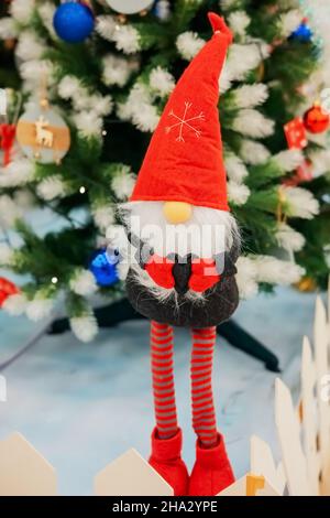 Un fabuleux gnome en peluche sur de longues jambes se tient sur le fond d'un élégant arbre de Noël.Carte de fête. Banque D'Images