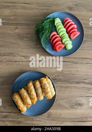 Une table de petit-déjeuner turque classique est vue en gros plan. De délicieux rouleaux de printemps faits maison, des tomates fraîches et des concombres sont préparés sur des assiettes. Banque D'Images
