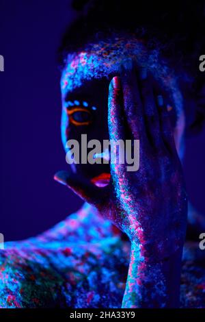 jeune femme noire avec des gravures fluorescentes sur la peau, peinture cosmique brillante sur les lumières néon, fond noir en studio. femelle avec moitié de fermeture d'art du corps Banque D'Images