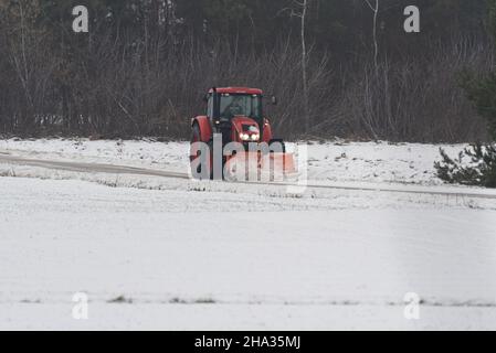 Putusk, Pologne - 10 décembre 2021 : déneigement d'une route rurale avec un tracteur équipé d'un chasse-neige. Banque D'Images