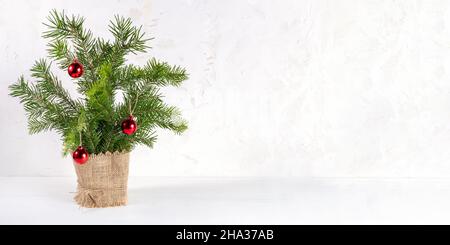 Bannière moderne tendance blanche de Noël minimaliste avec bouquet de branches de sapin décorées de boules de Noël rouges et de burlap comme petit arbre de Noël alternatif.Hol Banque D'Images