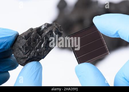 Charbon à côté du panneau solaire dans les mains des scientifiques en laboratoire.Le concept de transition entre les combustibles fossiles et les énergies renouvelables vertes. Banque D'Images