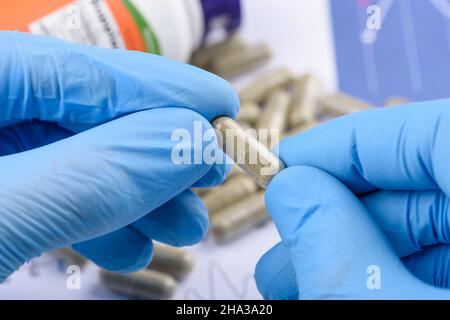 Capsule de supplément transparente dans les mains des scientifiques, bouteille et pilules sur le fond. Banque D'Images