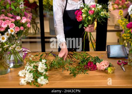 Fleuriste au travail: Femme caucasienne de culture organisant des décorations florales, faisant un bouquet pour les clients. Adorable dame en tablier est debout derrière le travail de bureau Banque D'Images