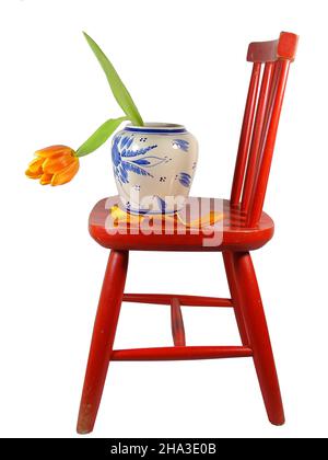 Une tulipe orange dans un vase sur une chaise rouge avec un fond blanc Banque D'Images