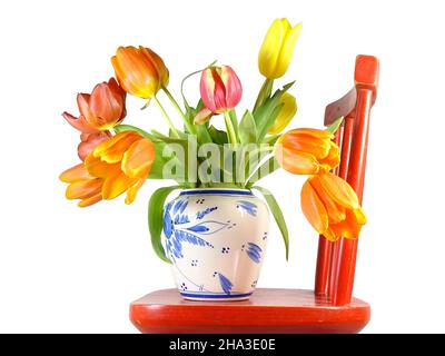 Un bouquet de tulipes de couleur dans un vase sur une chaise rouge à fond blanc Banque D'Images