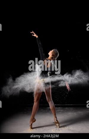 Ballerine dansant avec de la farine sur fond noir studio.Danseur en bodysuit noir dansant avec élégance avec de la farine.Pousse-photo en poudre.Port pleine longueur Banque D'Images