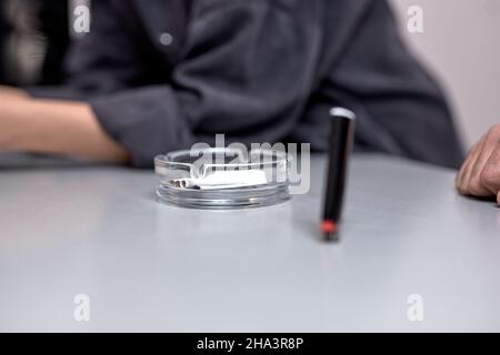 cendrier avec cigarette et allume-cigare en gros plan. gros plan sur cendrier. petit homme non reconnaissable assis en arrière-plan. concept de style de vie malsain Banque D'Images