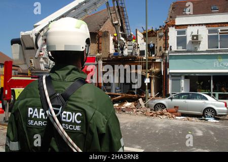 Un paramédic analyse un bâtiment endommagé à la suite d'une explosion alors que des pompiers travaillent dans les débris. Banque D'Images