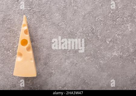 Un morceau de fromage Maasdam avec de grands trous sur fond de béton gris. Gros plan Banque D'Images