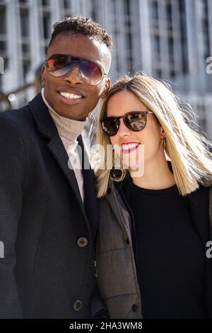 Optimiste divers homme et femme dans des vêtements d'extérieur et des lunettes de soleil tendance souriant et regardant loin pendant la date le jour ensoleillé dans la ville Banque D'Images