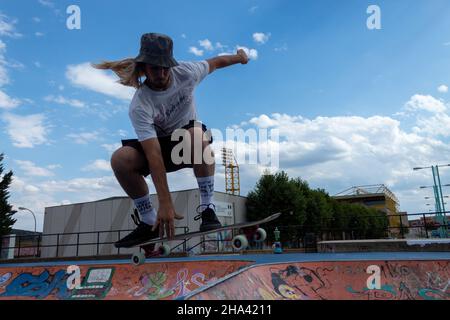 Jeune garçon blond patineur hispanique à poil long pratiquant le skateboard et le saut avec son skateboard Banque D'Images