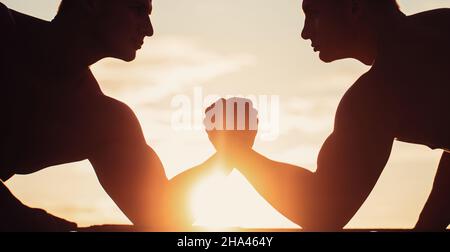 Rivalité, vs, défi, lutte de main. Coucher de soleil, lever du soleil. Hommes mesurant les forces, les bras. Deux hommes luttant. Silhouette de mains qui rivalisent Banque D'Images