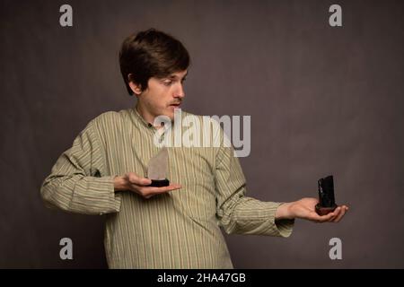 Jeune beau grand homme blanc mince avec des cheveux bruns tenant des cristaux blancs et noirs maintenant le noir loin sur fond gris Banque D'Images