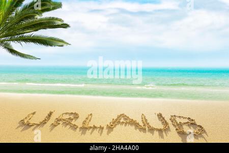 le mot vacances écrit dans le sable sur une plage de mer du sud Banque D'Images