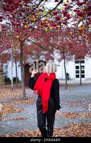 Jeune femme européenne blanche marchant avec des cheveux blonds en foulard rouge en automne Banque D'Images