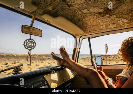 jeune femme utilisant un téléphone mobile penchée en voiture avec les jambes sur le tableau de bord. femme messagerie texte téléphone mobile. en voyage. femme touriste assis en voiture en utilisant le téléphone tout en se reposant les pieds sur le tableau de bord Banque D'Images