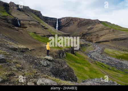 vue aérienne un homme en manteau jaune appréciant la cascade de hengifoss en islande. Banque D'Images