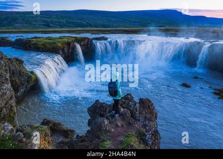 la vue aérienne d'une femme qui profite de la magnifique cascade de godafoss à la lumière du coucher du soleil. islande en été. Banque D'Images