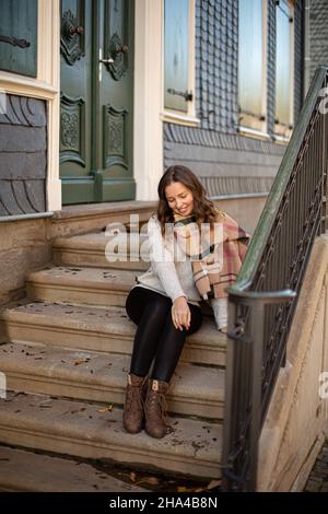 Assis jeune femme avec des cheveux bouclés dans un cavalier gris près du vieux bâtiment avec des escaliers Banque D'Images