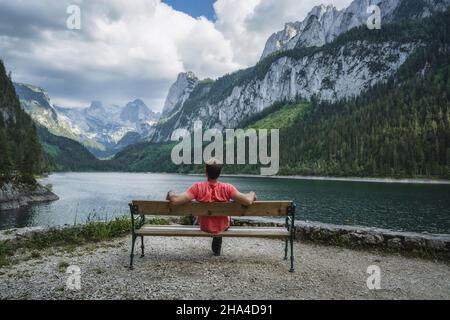 homme se reposant sur un banc en face des montagnes de dachstein reflétées dans le lac de gosau, autriche. Banque D'Images