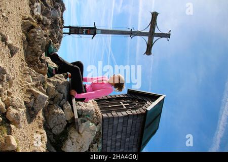 jeune femme prend une pause au sommet, randonnée à geigelstein (1808m), croix de sommet, chapelle, réserve naturelle, aschau im chiemgau, haute-bavière, bavière, allemagne Banque D'Images