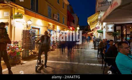 grèce,iles grecques,iles ioniennes,lefkada ou lefkas,ville de lefkada,capitale,humeur du soir,zone piétonne,longue exposition,personnes floues,homme sur scooter,éclairage artificiel de rue Banque D'Images