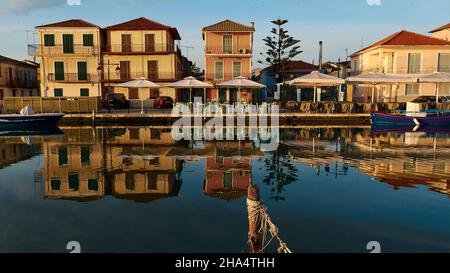 grèce,iles grecques,iles ioniennes,lefkada ou lefkas,ville de lefkada,capitale,lumière du matin,aube,rangée de maisons frontally de l'avant,reflétée dans l'eau calme du canal,poteau en bois au premier plan Banque D'Images