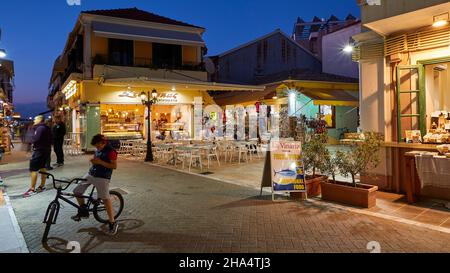 grèce,iles grecques,iles ioniennes,lefkada ou lefkas,ville de lefkada,capitale,crépuscule,ciel bleu minuit,zone piétonne,feux de rue,garçon sur vélo en premier plan à gauche,parlant sur téléphone mobile Banque D'Images