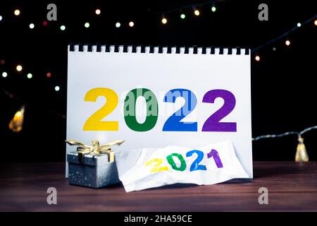 2022 concept de médecine. Chiffres sur une feuille de papier avec un masque médical, des gants, sur fond de guirlandes de Noël brûlantes. Banque D'Images