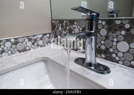 Vue rapprochée d'un robinet d'évier à l'intérieur d'une salle de bains haut de gamme, l'eau courante du robinet Banque D'Images