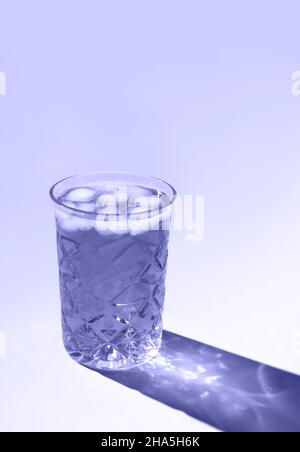 Le magnifique verre en cristal projette une ombre longue de la lumière du soleil.Coloris tendance de l'année 2022.Composition créative minimale avec espace de copie.Concept des boissons d'été. Banque D'Images