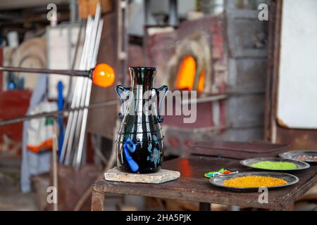 Un artisan vénitien en verre de l'île de Murano travaille sur un vase en verre soufflé sur une table de travail en fer avec une tige en métal. Venise, Italie. Banque D'Images