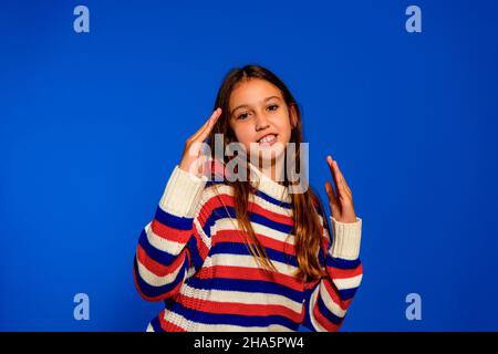 Petite fille hispanique portant une chemise à manches longues sur fond bleu poing de Punching pour combattre, agressif et en colère attaque, menace et violence. Banque D'Images