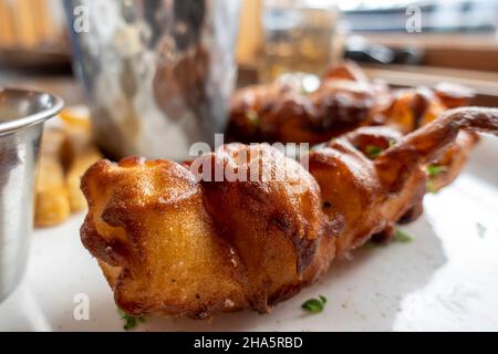 Gros plan de filets de poisson dorés et battus avec des frites épaisses sur une assiette avec ketchup, sauce tartare et vinaigrettes de ranch à l'intérieur d'un restaurant Banque D'Images