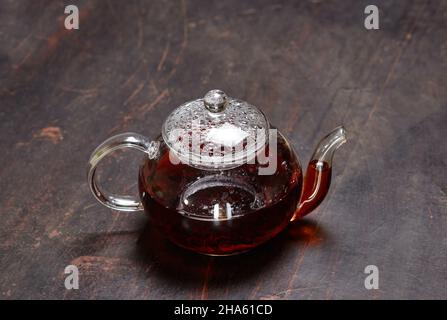 Thé noir dans une théière en verre sur fond de bois.Thé noir fraîchement préparé dans la vaisselle sur table de cuisine sombre avec espace pour les copies Banque D'Images