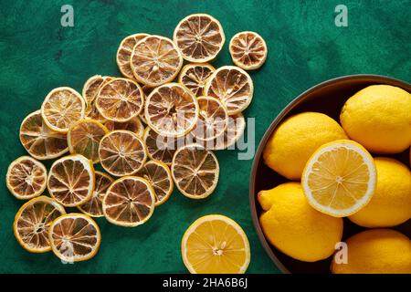 Citron séché sur fond vert avec citron frais dans un bol en bois. Banque D'Images