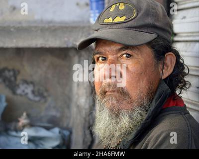 Un homme mexicain âgé et robuste, sans abri, avec une barbe grise et des cheveux en forme de vaisselle, porte une casquette de baseball usée et regarde le spectateur. Banque D'Images