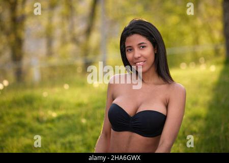 Femme colombienne confiante posant à l'extérieur en Jean denim et haut noir entouré par la lumière du soleil et des arbres à Toronto, Canada. Banque D'Images