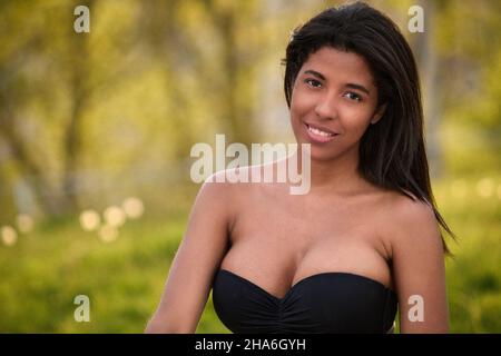 Jeune femme colombienne souriant avec confiance dans le top crop top noir et Jean denim à l'extérieur dans le parc ensoleillé de Toronto, Canada. Banque D'Images
