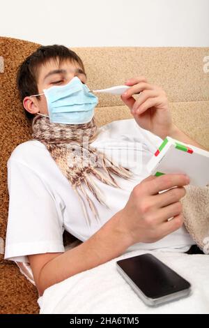 Adolescent malade dans le masque de grippe avec un paquet de pilules sur le canapé à la maison Banque D'Images