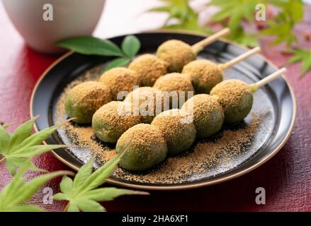 Boulettes de riz aromatisées à l'armoise recouvertes de farine de soja et de thé vert servies sur une assiette noire placée sur un plateau rouge boulettes japonaises. Banque D'Images