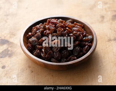Raisins secs dans un bol en bois placé sur un vieux fond en bois. Banque D'Images