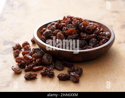 Raisins secs dans un bol en bois placé sur un vieux fond en bois. Banque D'Images