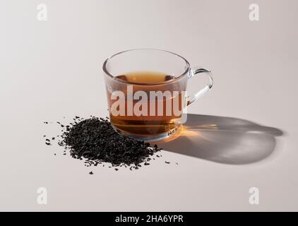 Thé chaud et feuilles de thé dans un verre sur fond beige Banque D'Images